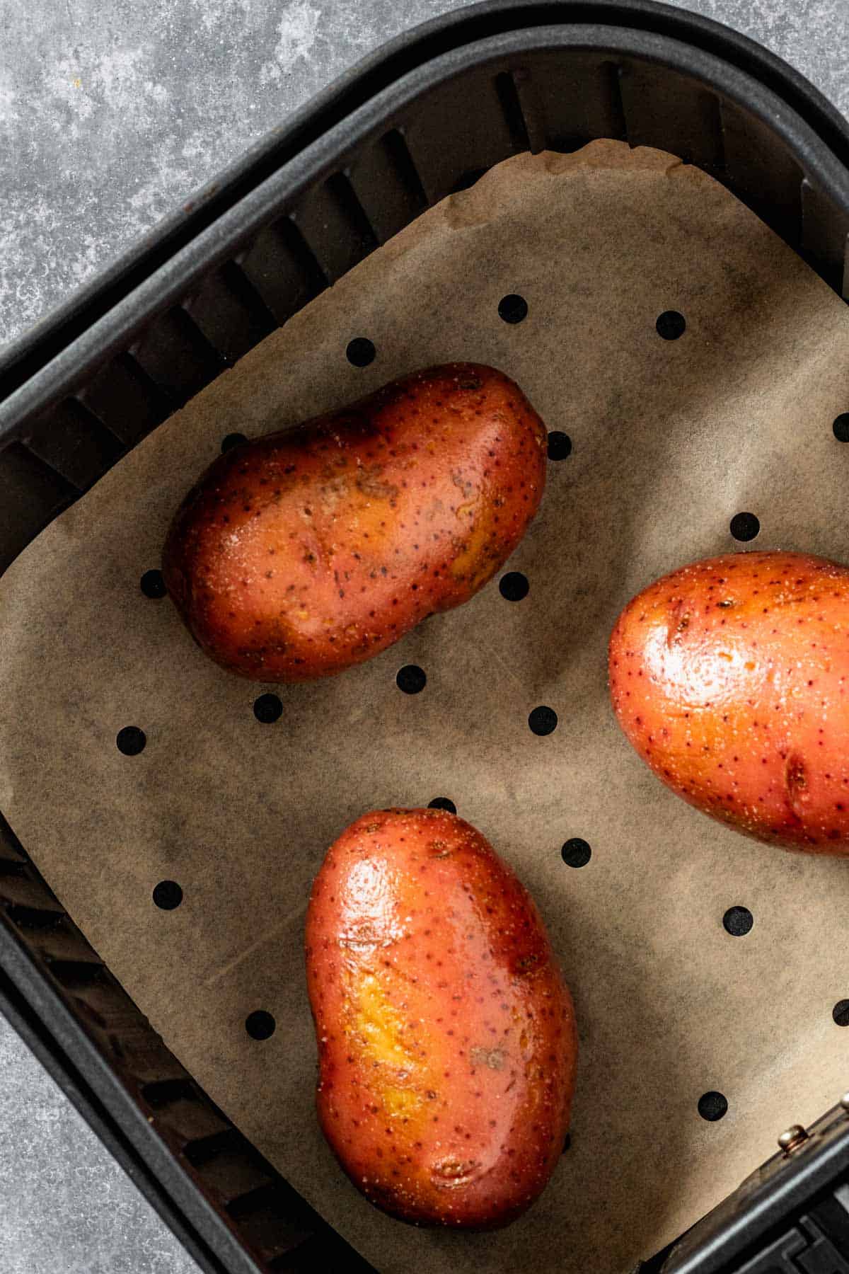 oily raw whole potatoes in air fryer basket.