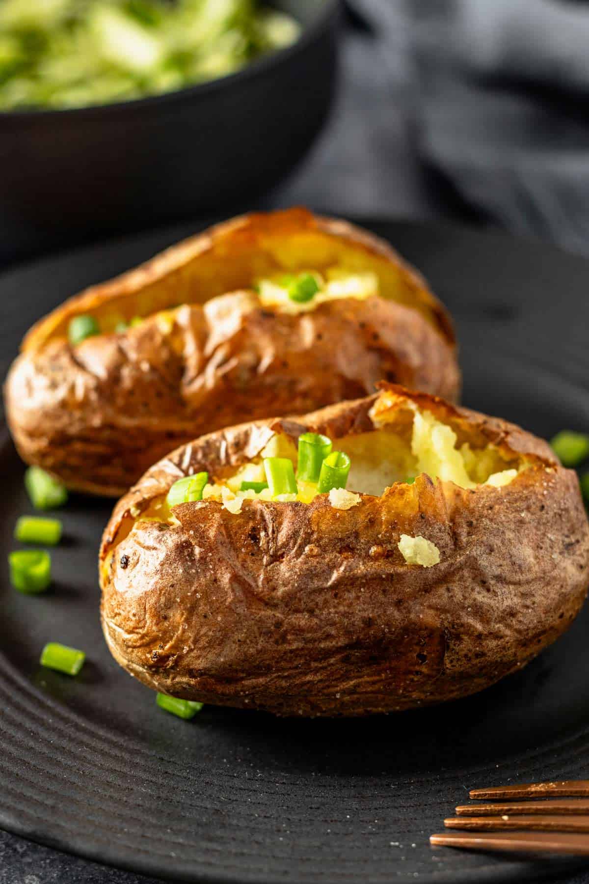 two air fryer baked potatoes cut in half topped with melting butter and chopped green onions.