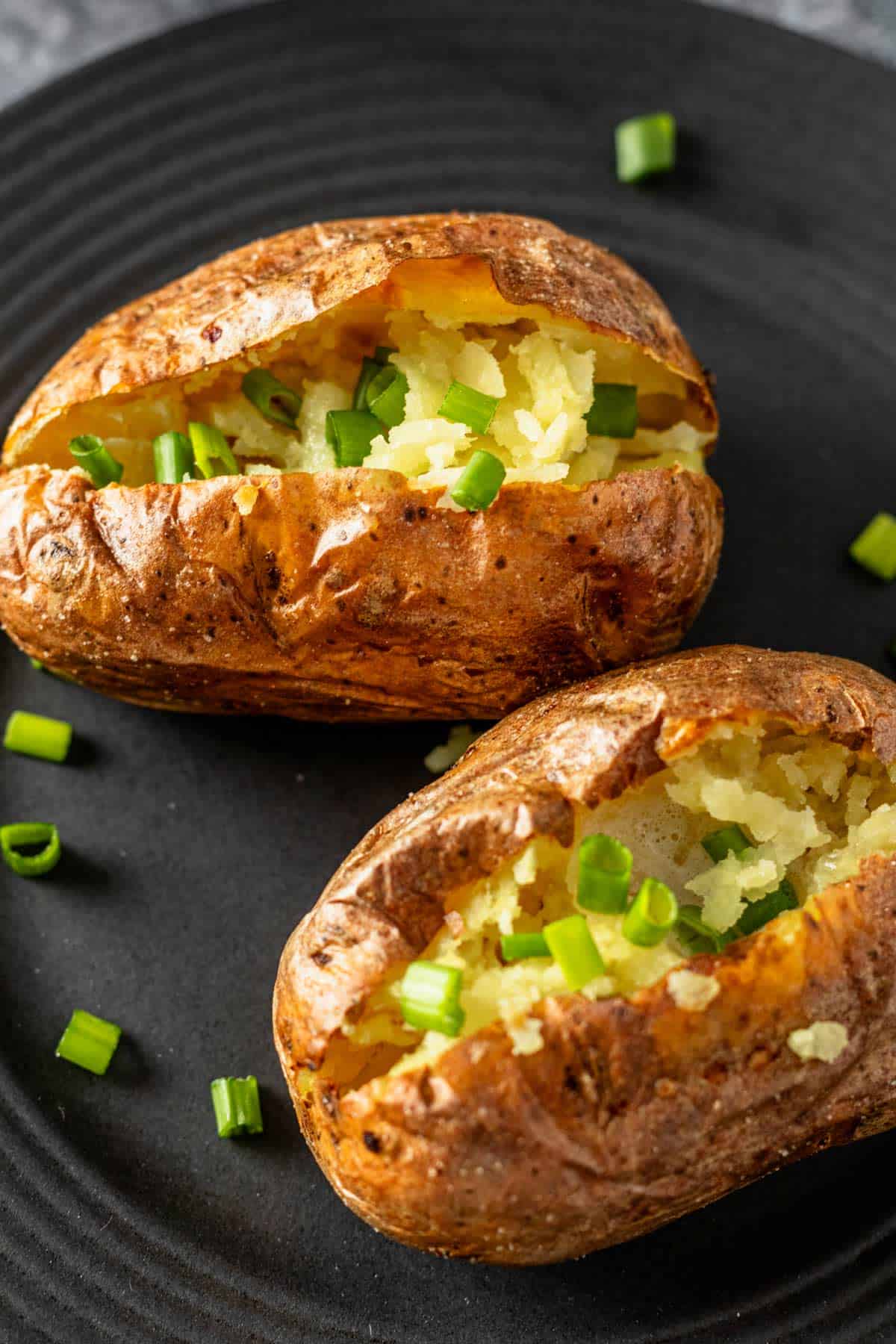 two air fryer baked potatoes cut in half topped with melting butter and chopped green onions.