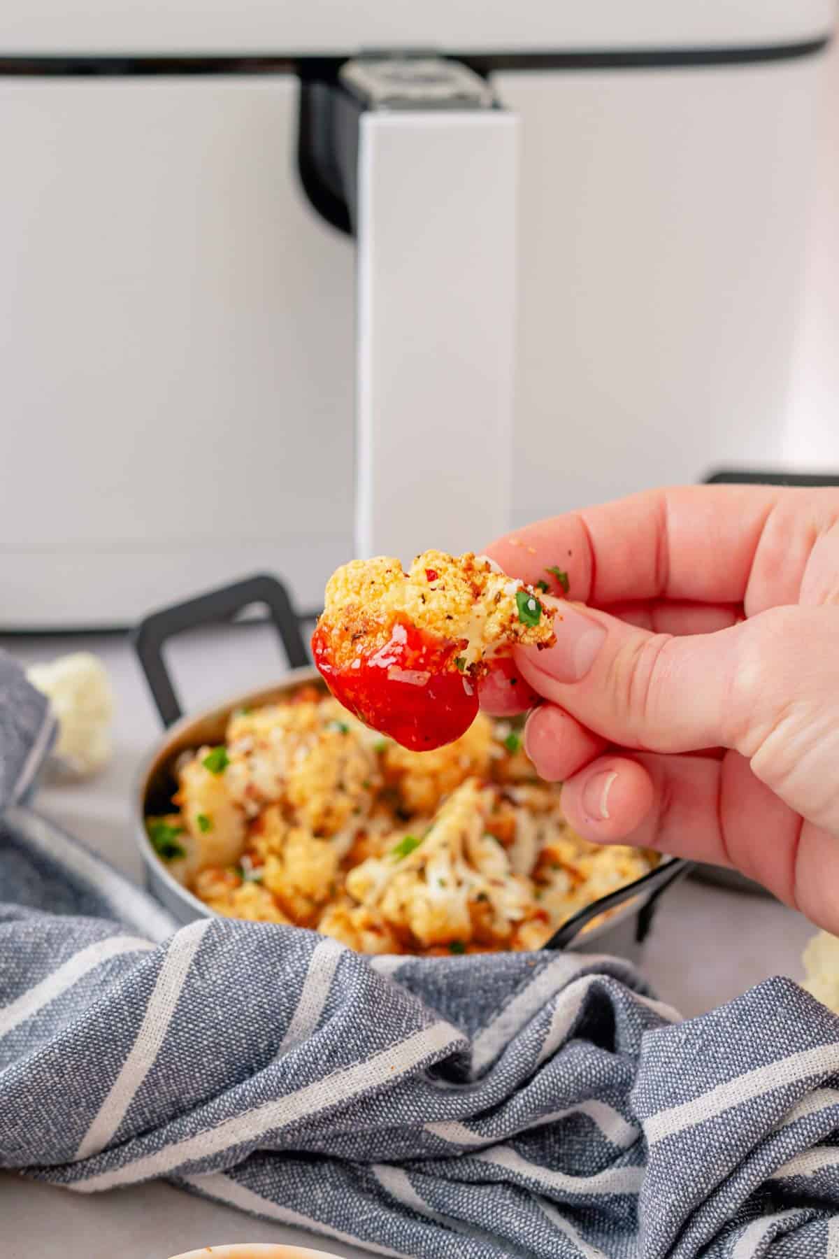 air fryer cauliflower in hand dipped in ketchup