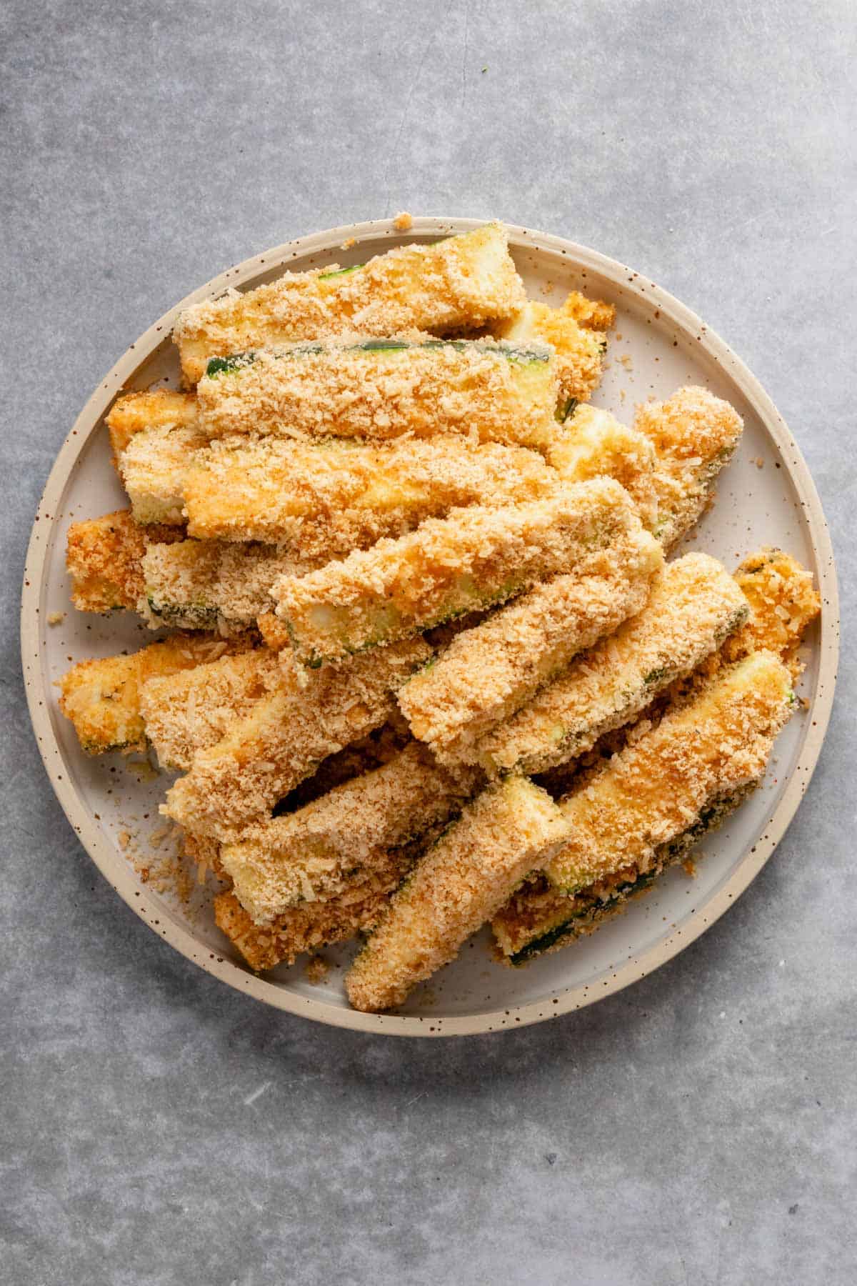 unbaked stack of breaded zucchini sticks on a plate.