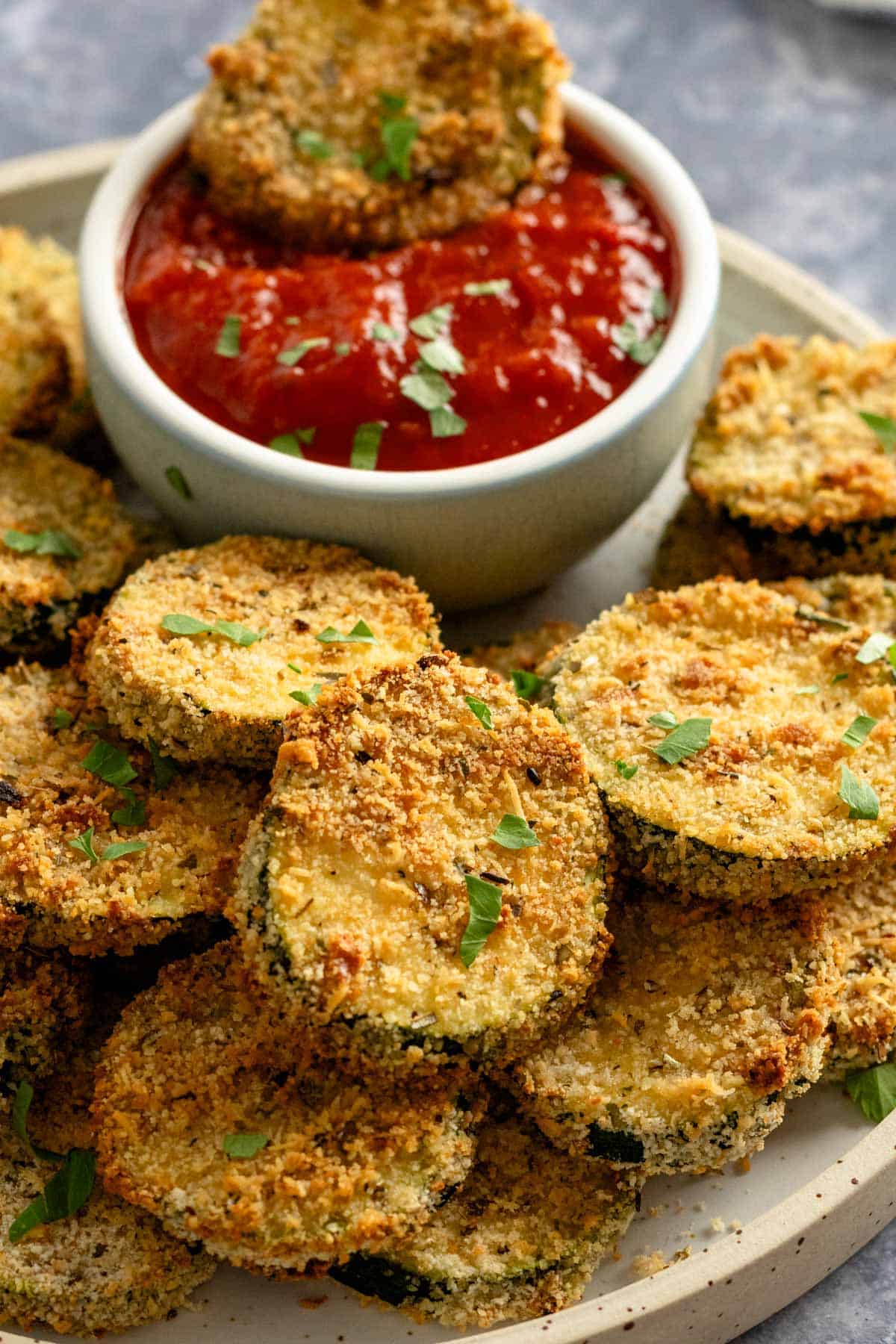 cooked air fryer zucchini slices on a bowl with red dipping sauce bowl.