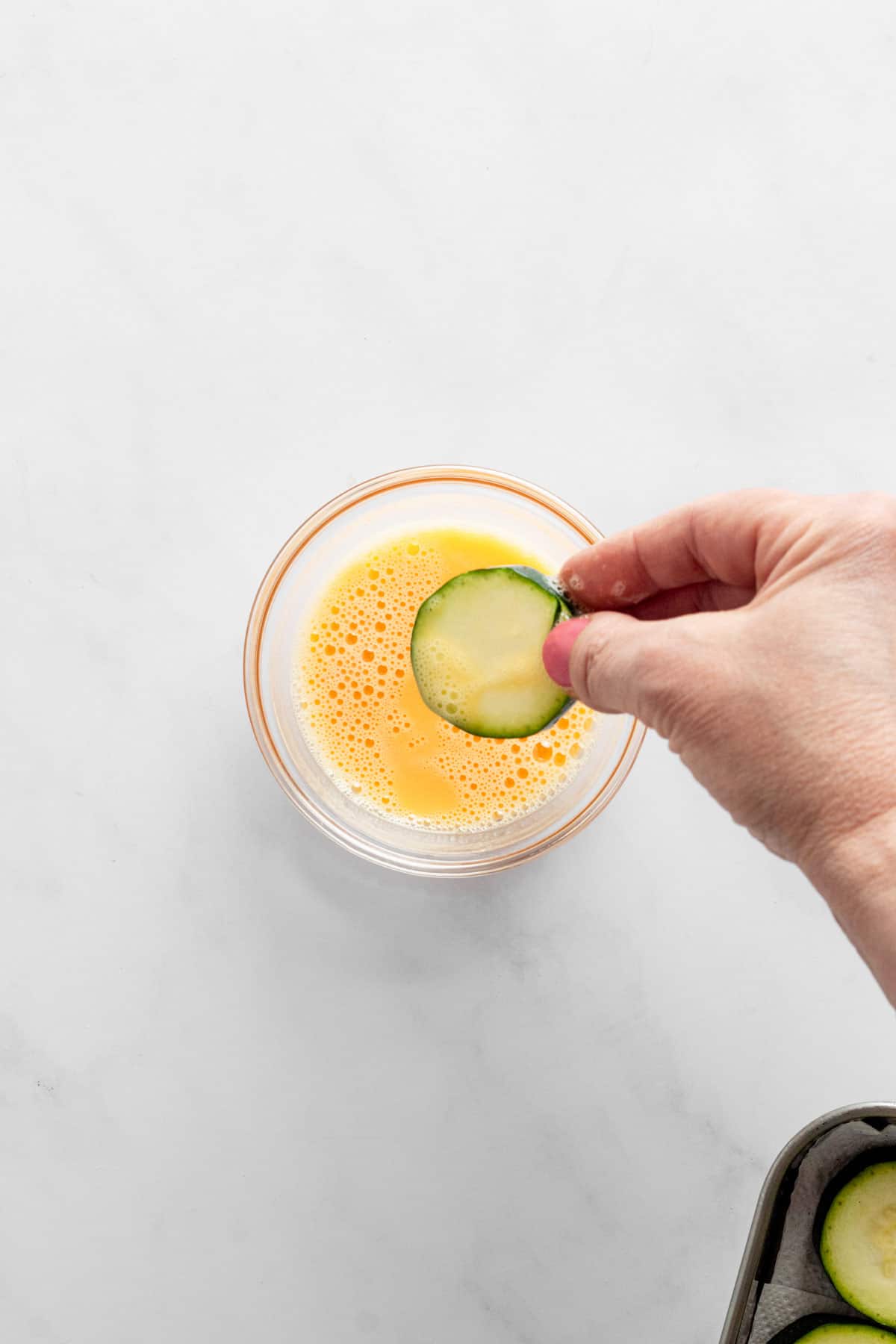 dipping zucchini into egg wash bowl.