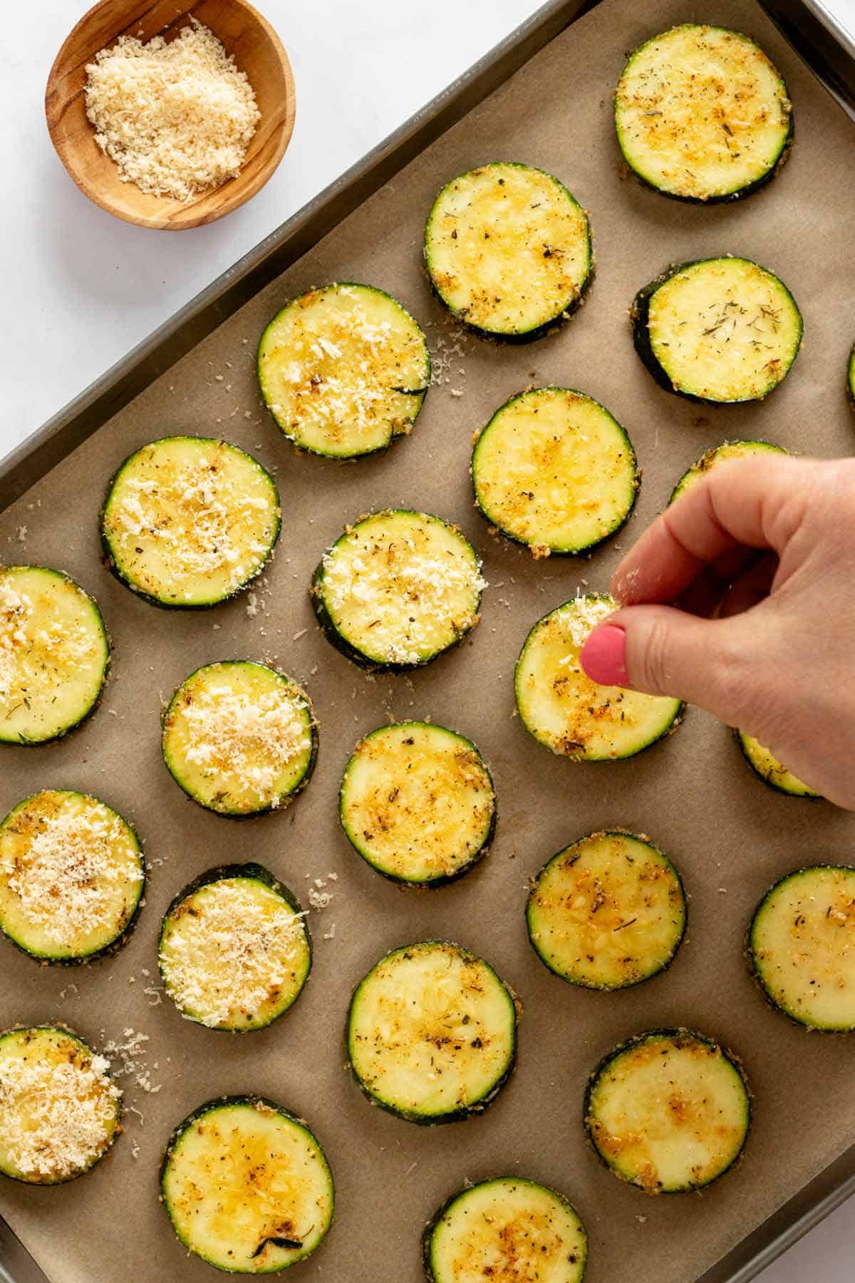 adding parmesan to zucchini slices on a baking sheet.