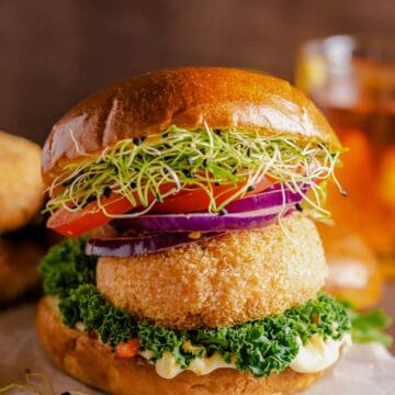 salmon patties served between burger buns, greens, tomato, red onion