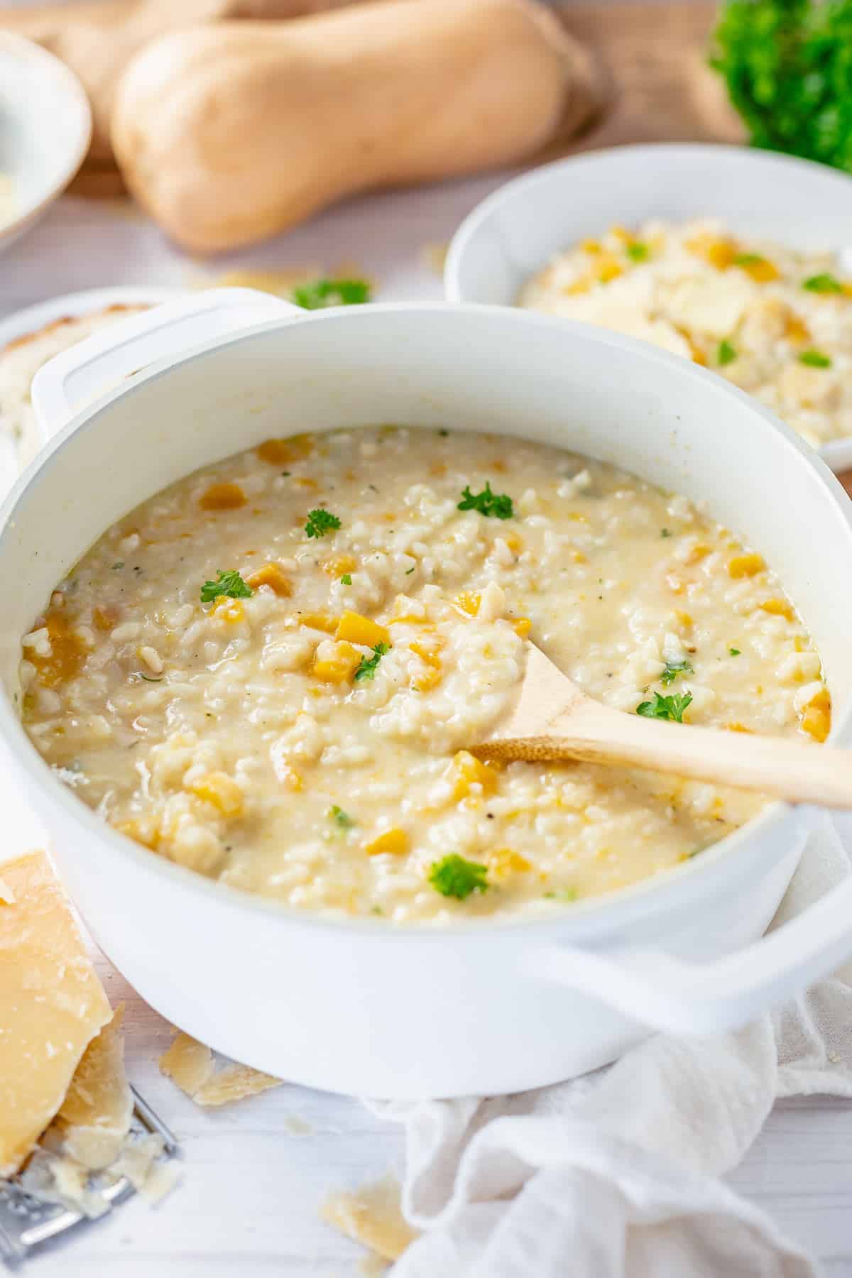 side view angle of a pot filled with pumpkin risotto and a wooden spoon inside