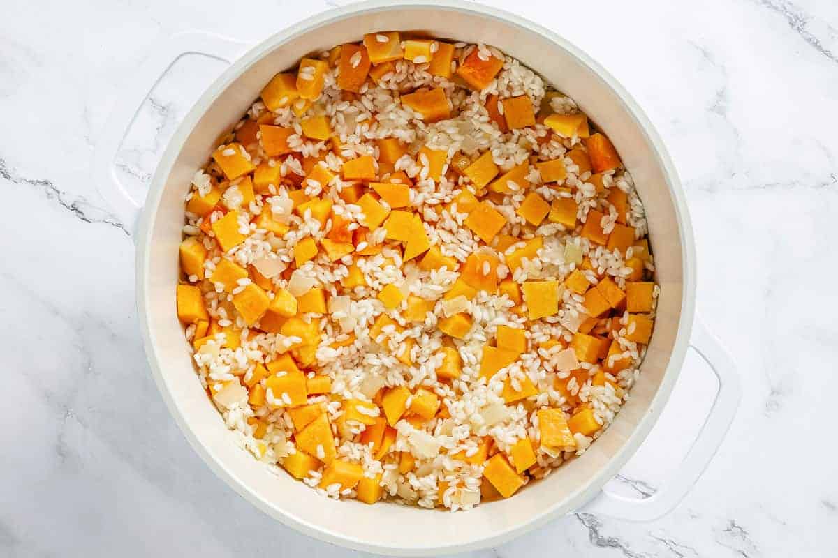 arborio rice and pumpkin pieces sauteeing in a white dutch oven