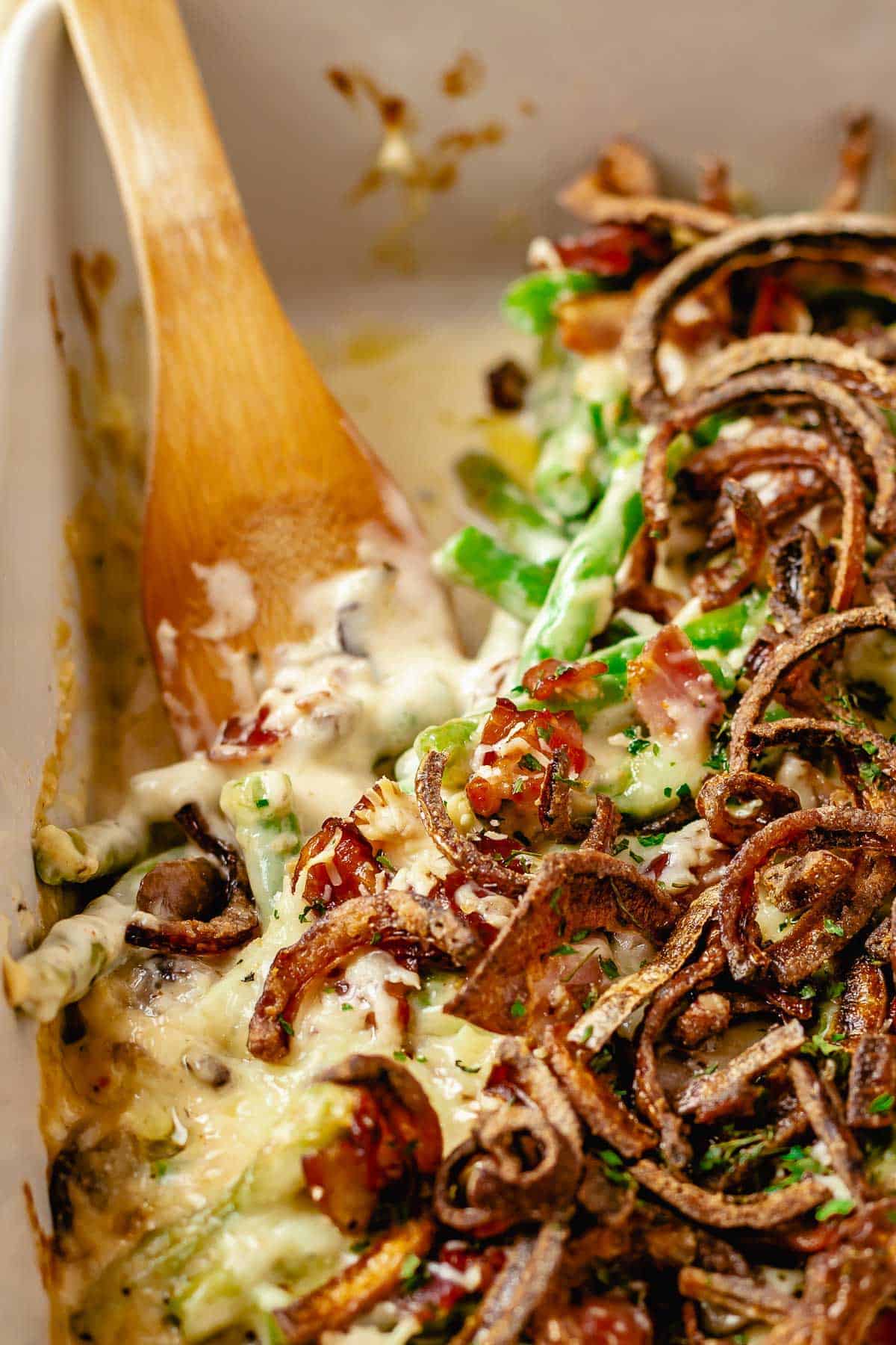 Close up shot of a wooden spoon placed in baked green bean casserole dish