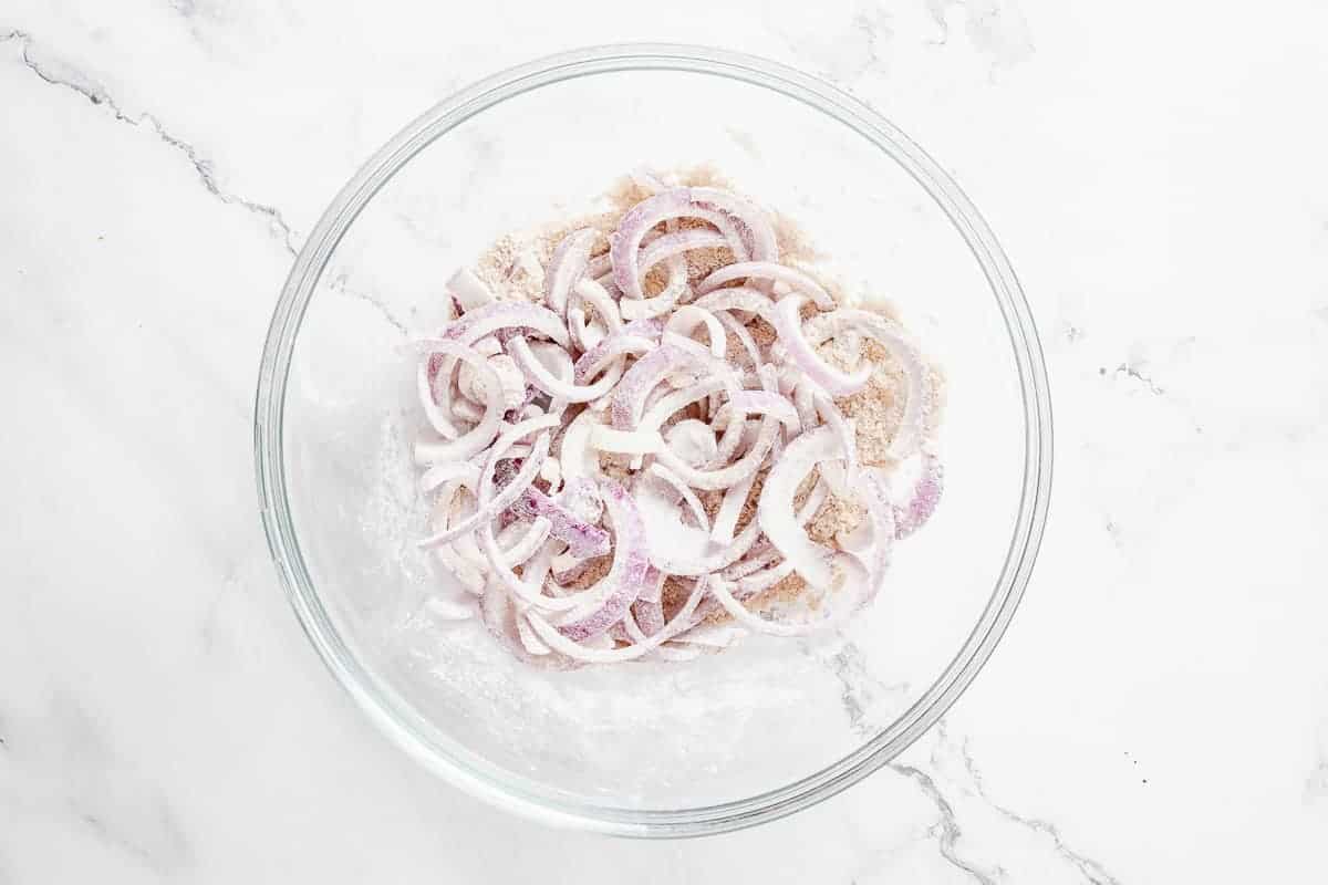 Sliced red onions tossed in flour and breadcrumbs mixture in a transparent glass bowl