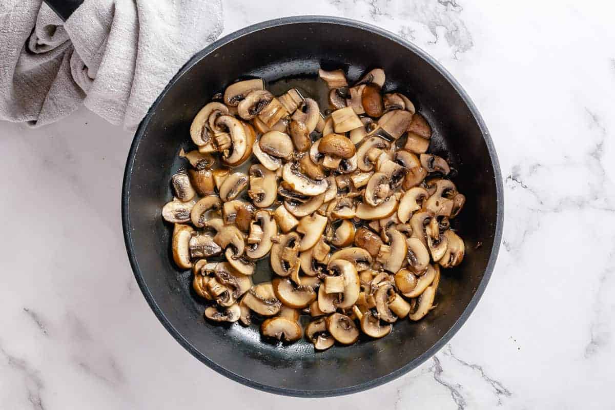 Sliced dark mushrooms frying in a black skillet