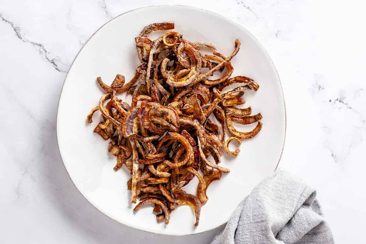 Crispy fried red onions resting on a plate after deep frying