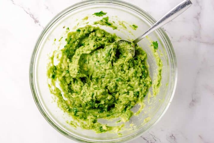 Simple guacamole in a white bowl with nacho chips around on a white marble background