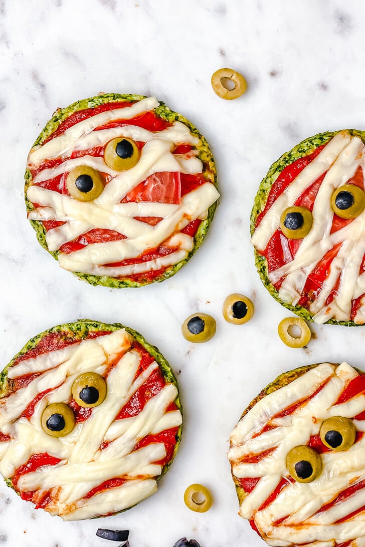 Halloween Mummy Pizzas - is the perfect Halloween party or dinner idea. Make these mummies with your kids for an easy and super flavorful Halloween themed meal. These mini pizzas are also gluten-free! The Yummy Bowl #savouryhalloweenfood #halloweenfoodrecipes #halloweenmummypizza #mummypizza #creepyhalloweenfoodideas #traditionalhalloweenfood #halloweentreats 