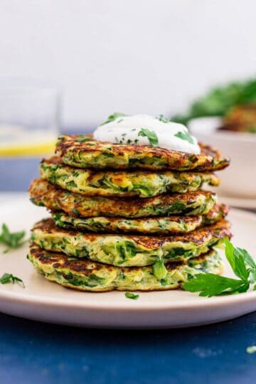 stack of zucchini fritters with a dollop of sour cream and parsley