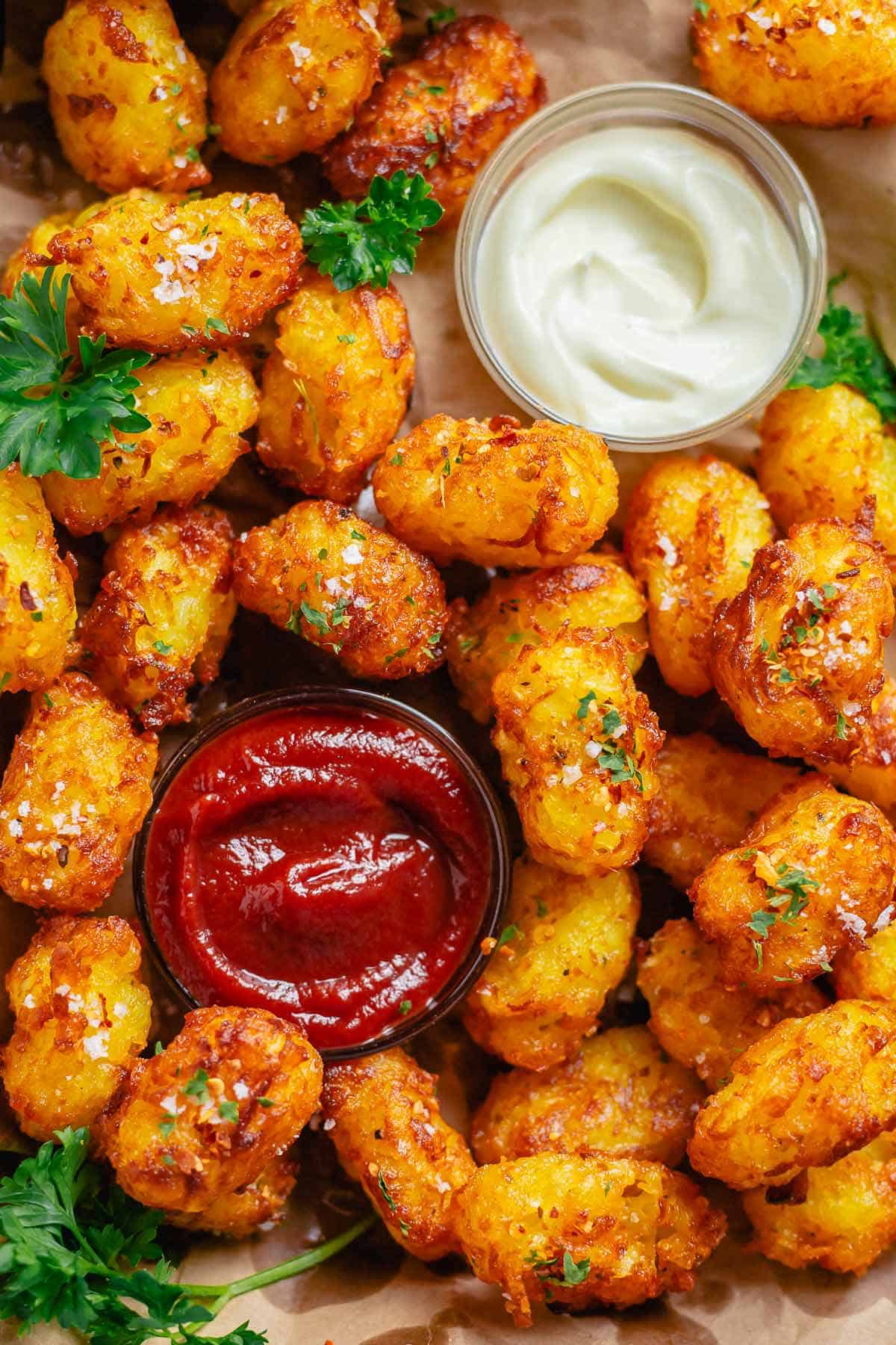 head shot of piled tater tots with a bowl of ketchup and mayonnaise