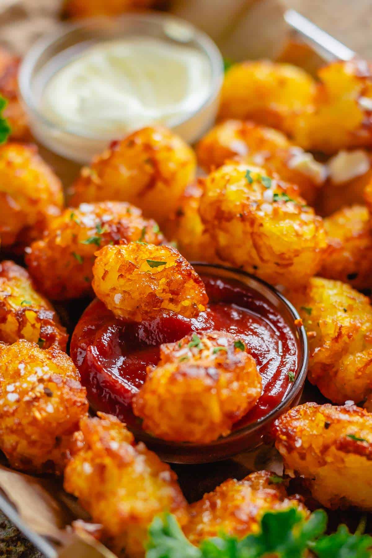 head shot of piled tater tots with a bowl of ketchup and mayonnaise