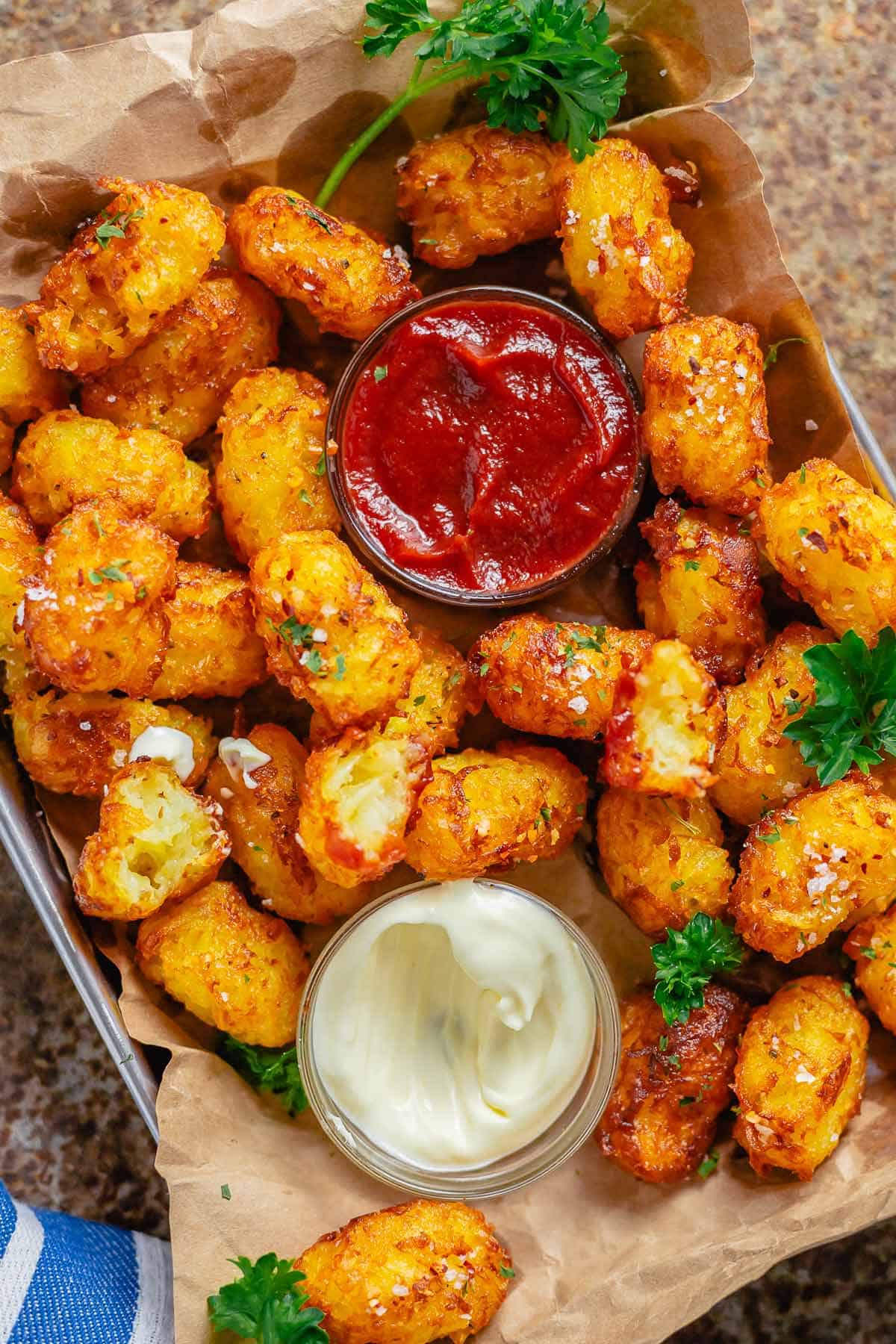 head shot of piled tater tots with a bowl of ketchup and mayonnaise