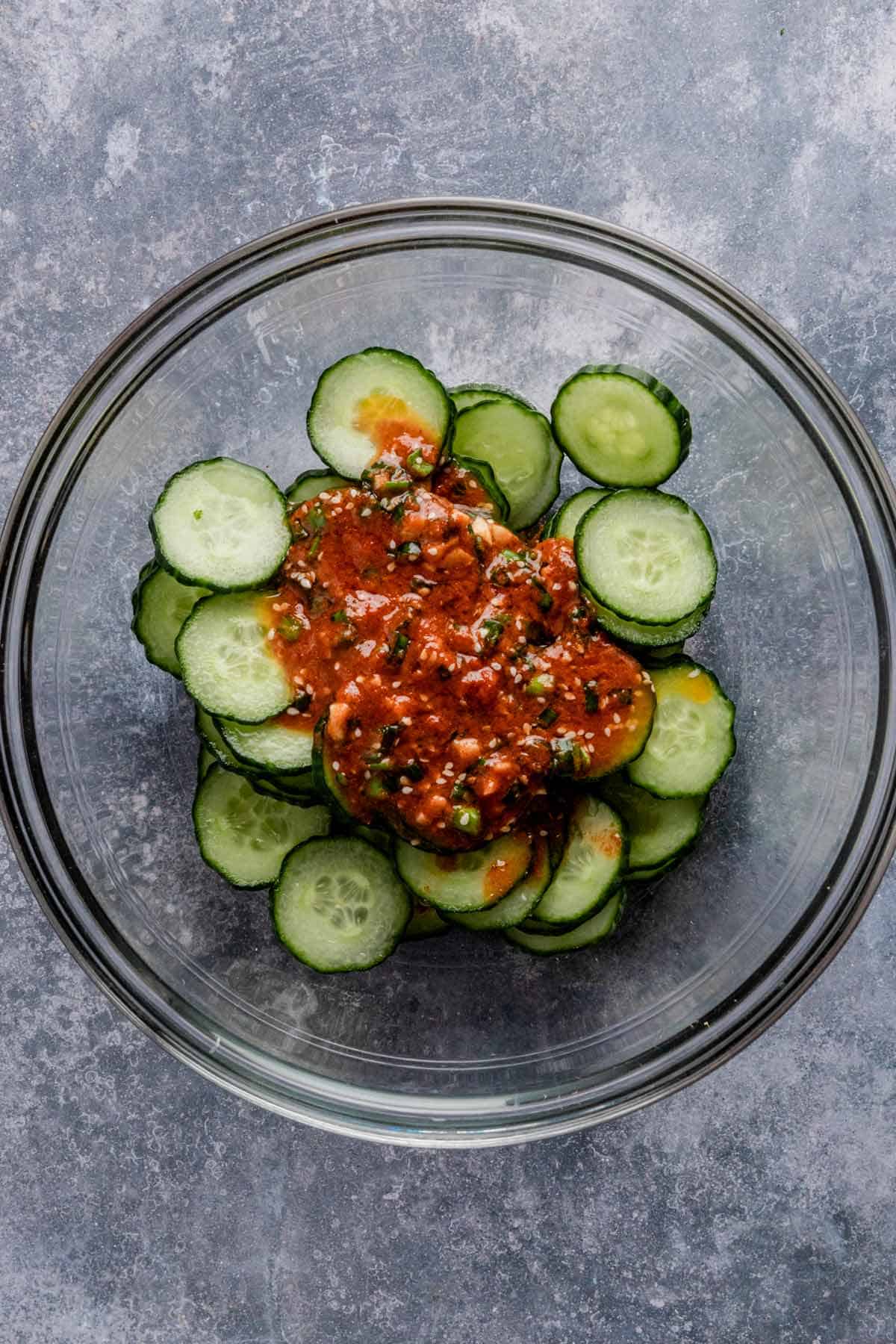 slices of cucumber in a bowl with red dressing on top