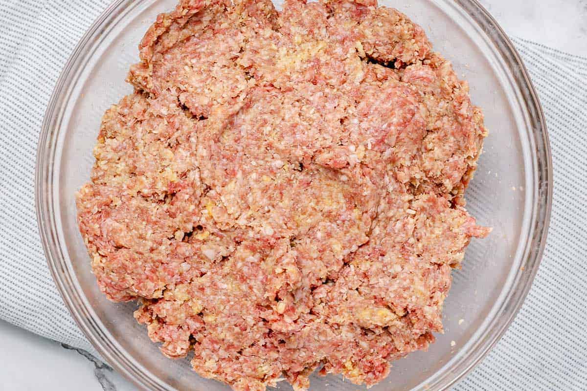 flatlay shot of a ground beef and pork mixed along with seasonings in a large glass transparent bowl