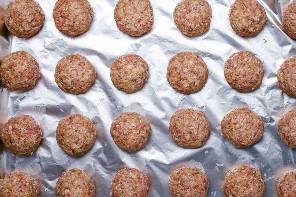 flatlay shot of 24 raw rolled meatballs on a baking sheet lined with foil