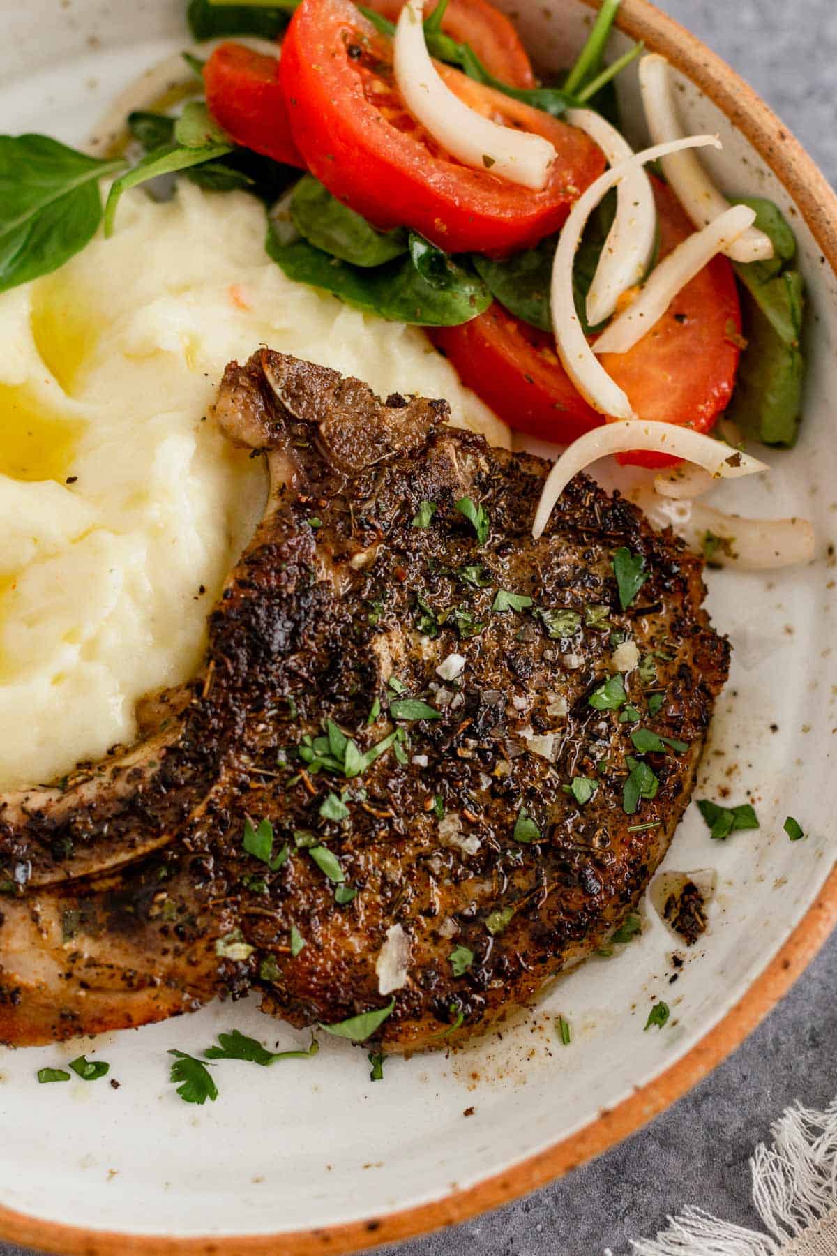 Pan Seared Pork Chop in a plate with mashed potatoes and tomato onion lettuce salad