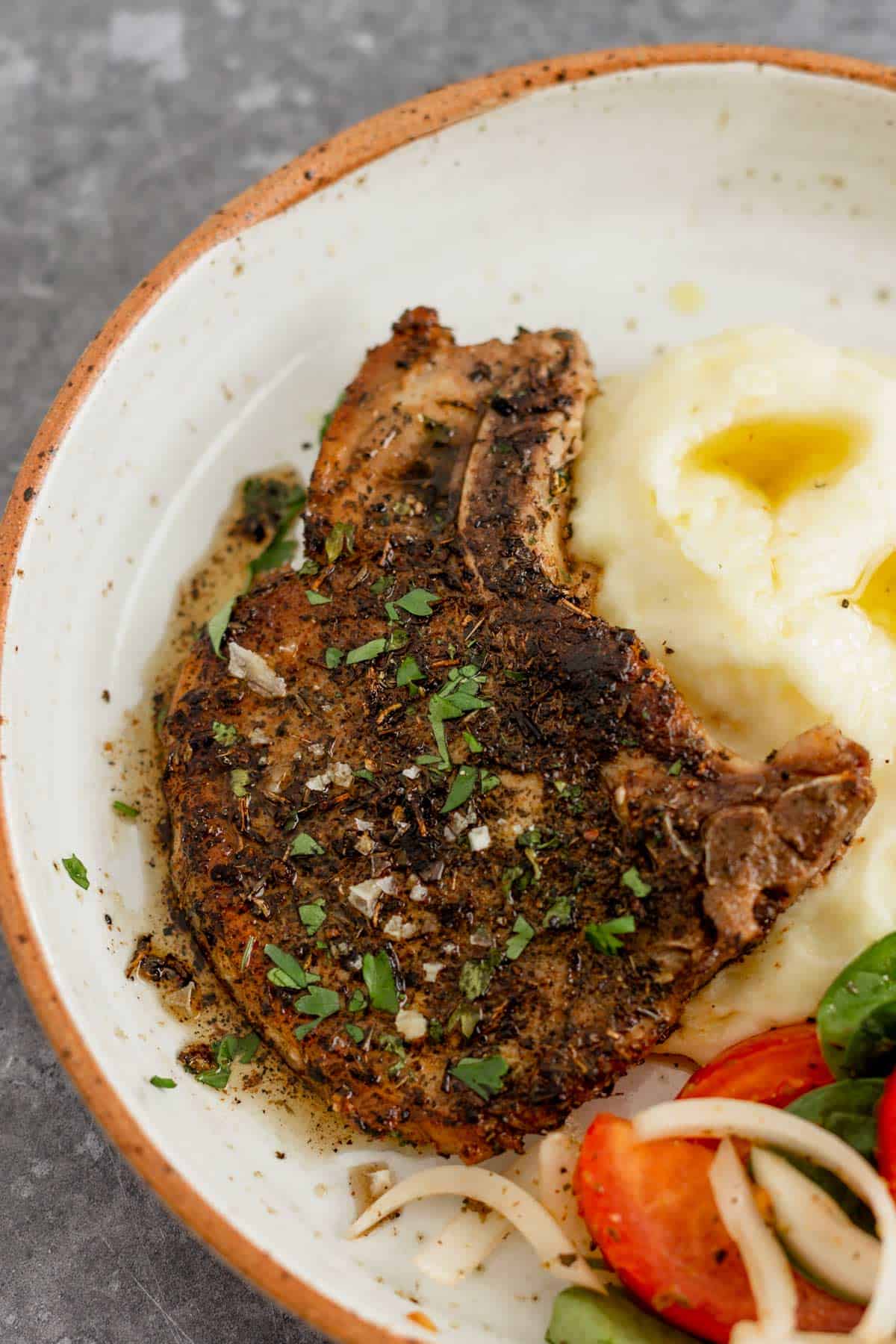 Pan Seared Pork Chop in a plate with mashed potatoes and tomato onion lettuce salad