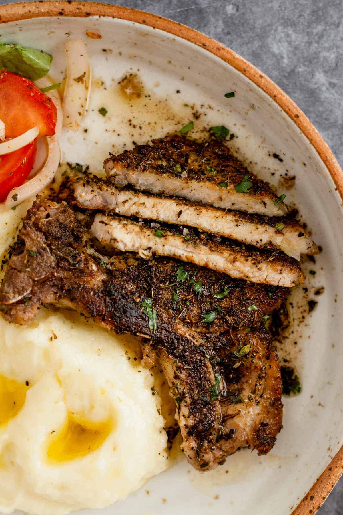 Pan Seared Pork Chop in a plate with mashed potatoes and tomato onion lettuce salad