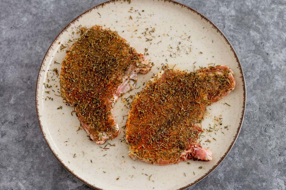 Pan Seared Pork Chops in a plate with dried herbs seasonings before cooking