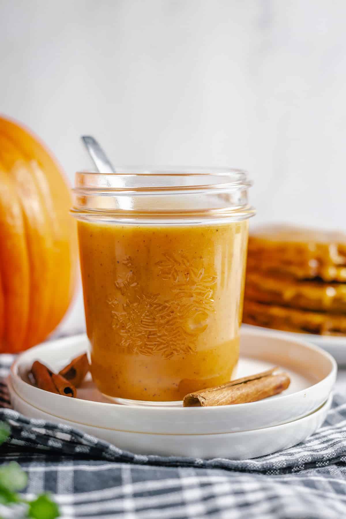 pumpkin caramel sauce in a jar with a pumpkin and pancakes background