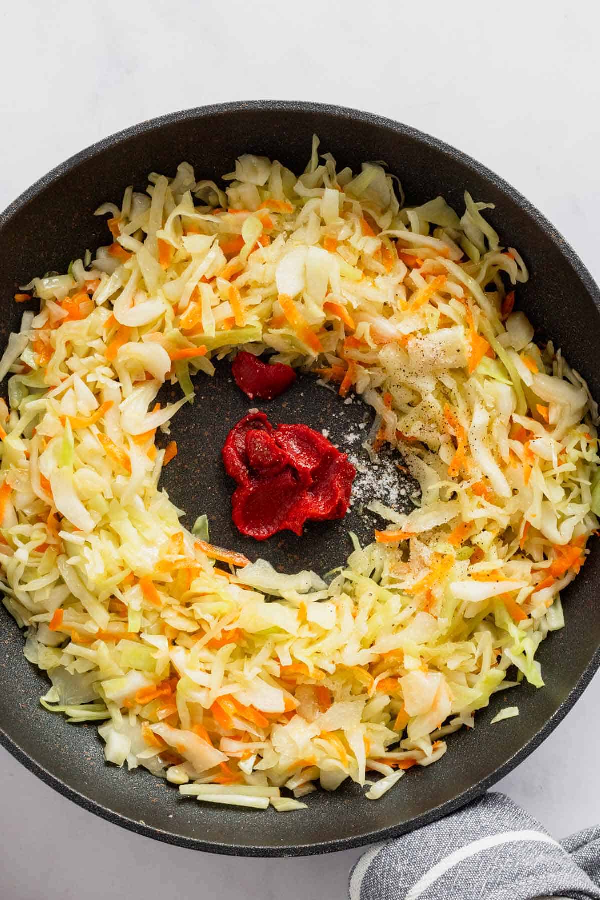 mixing tomato paste with cabbage in skillet.