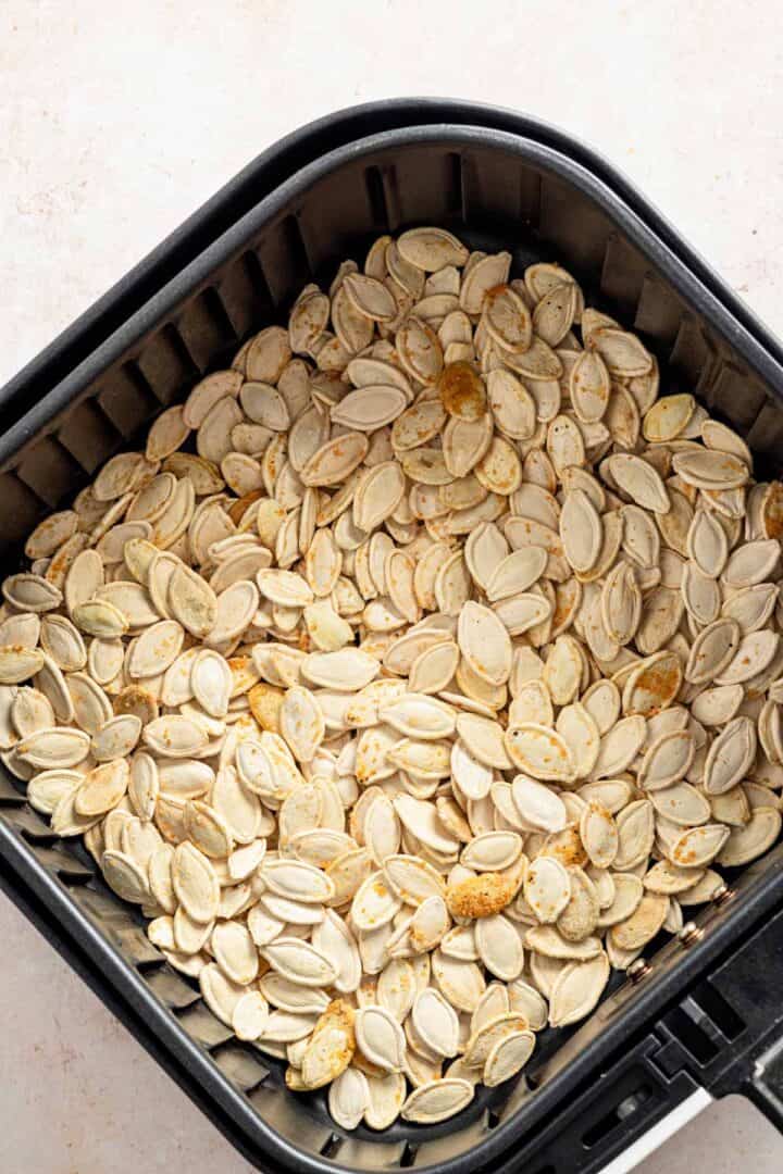 adding seasoned pumpkin seeds to air fryer basket.