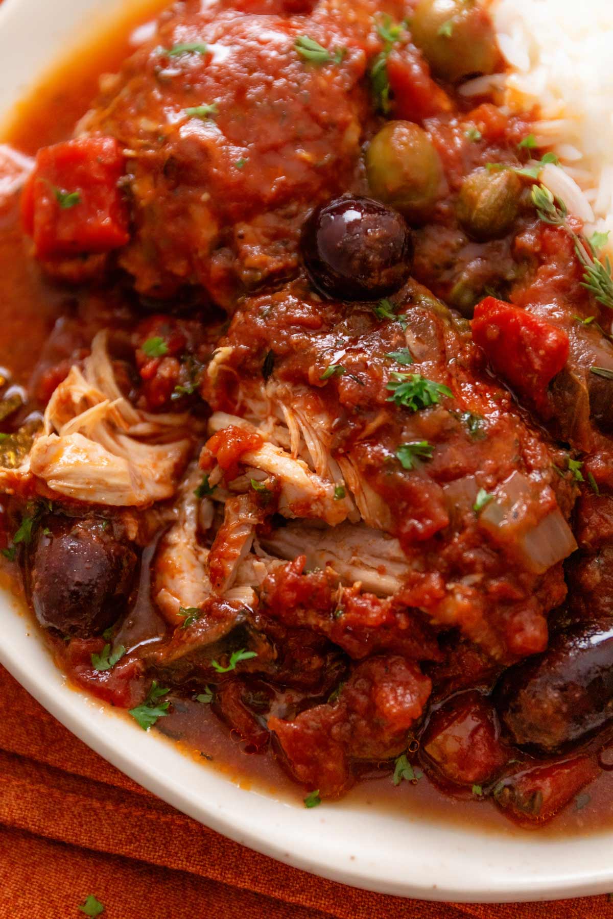 a close up shot of crock pot chicken thighs in tomato sauce and Italian seasonings and olives (Chicken Cacciatore)