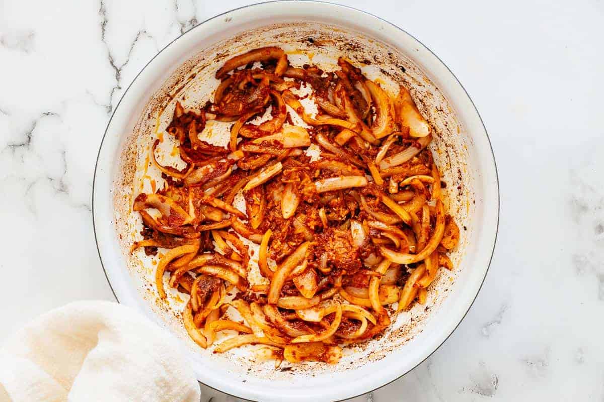 onion and red curry paste sauteing in a white pan