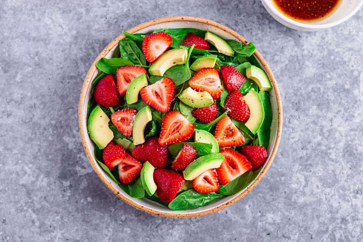 starwberries spinach and avocado in a salad bowl before adding the dressing