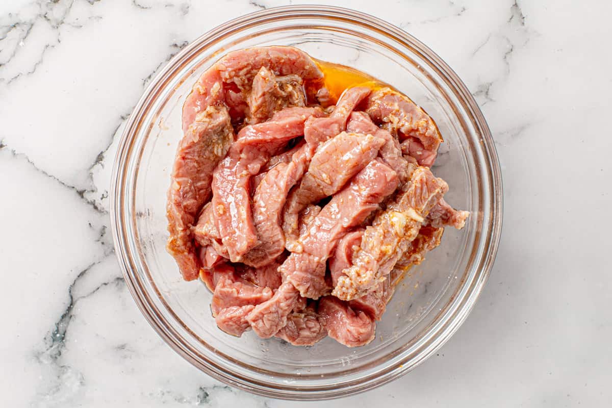 flank steak cut in strips marinating in a bowl with fajita seasoning