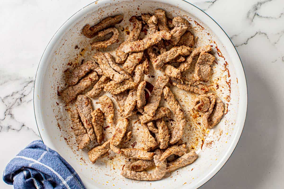 beef steak strips cooked in a white pan for fajita