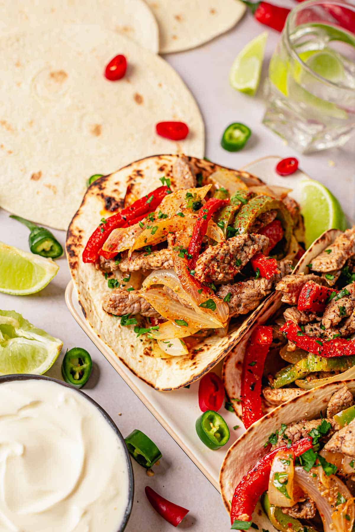 steak fajita tacos in a row with toppings and garnishes