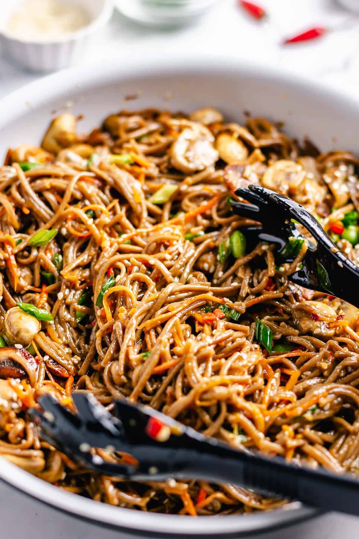 Stir Fry Soba Noodles with black kitchen tongs in a white skillet