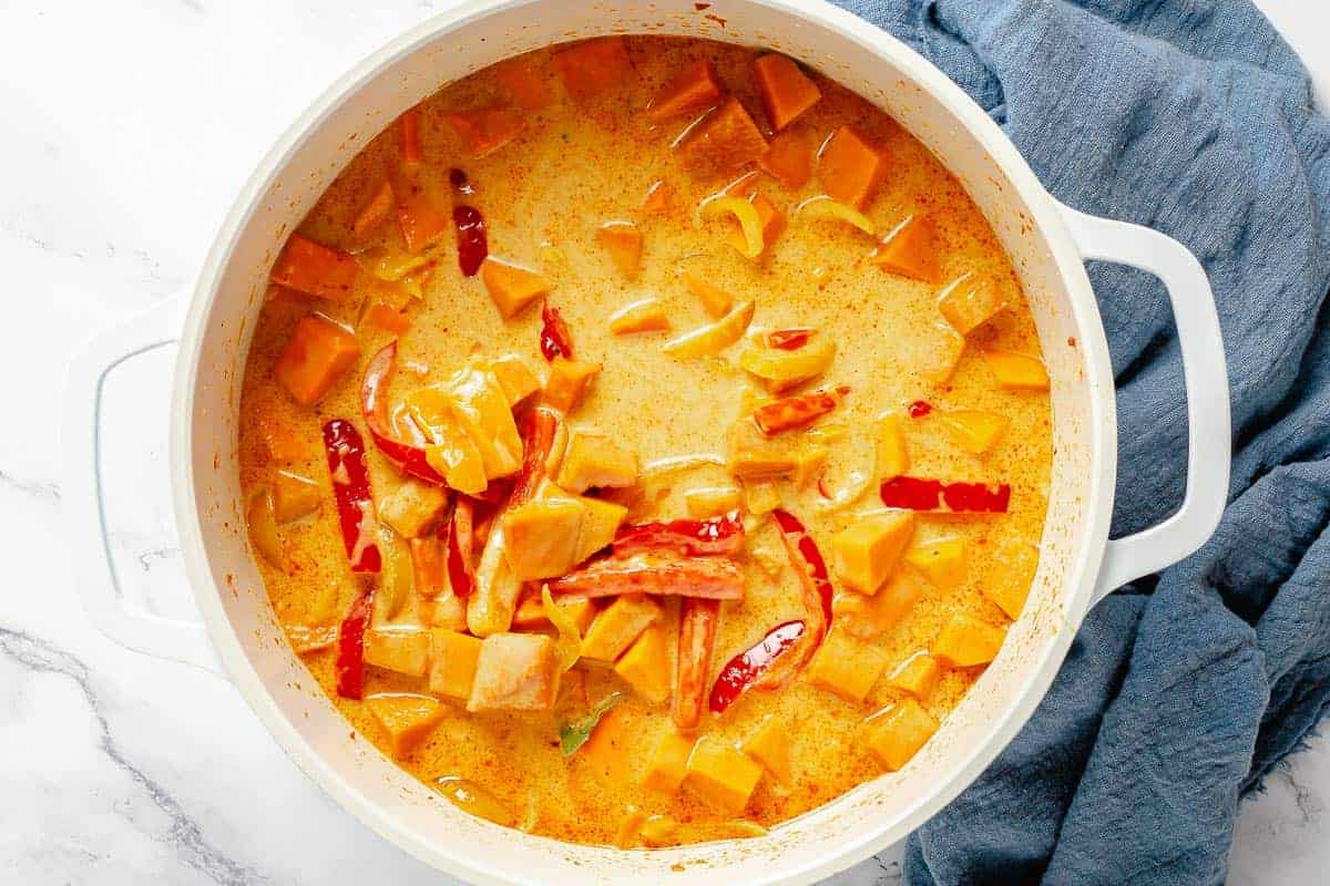 pumpkin curry ingredients simmering in a white pot along with coconut milk and vegetable broth