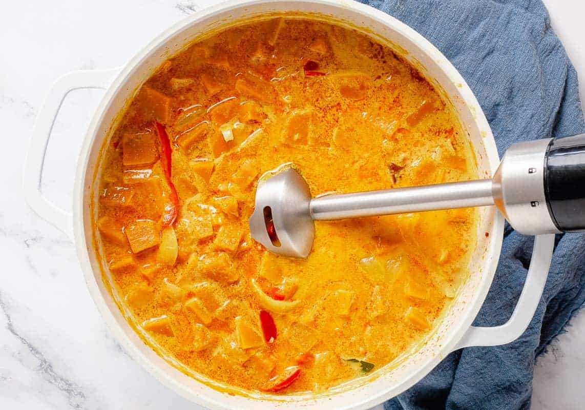 Immersion blender dipped into pumpkin curry pot