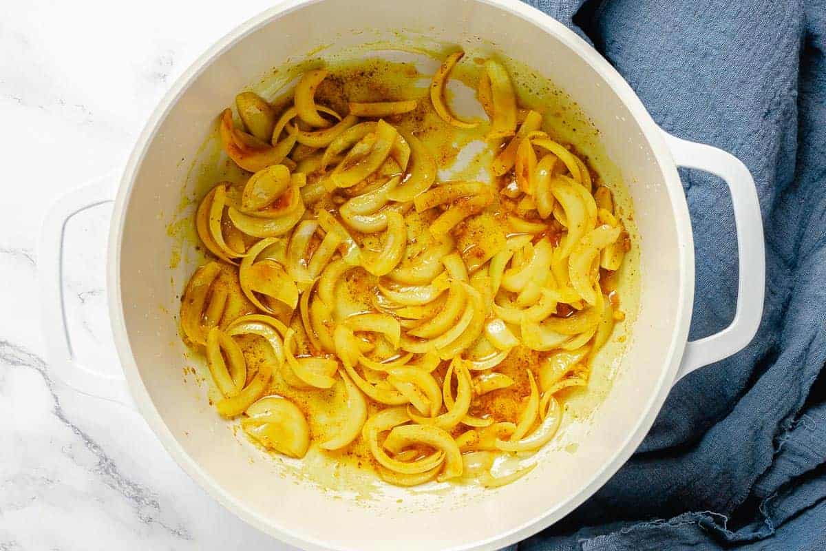 onion slices and spices cooking in a heavy bottom white pot