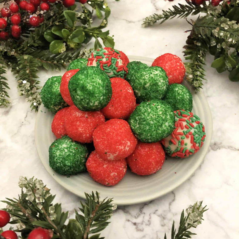 Red and green moscato truffle balls on a white plate with christmas decorations around them