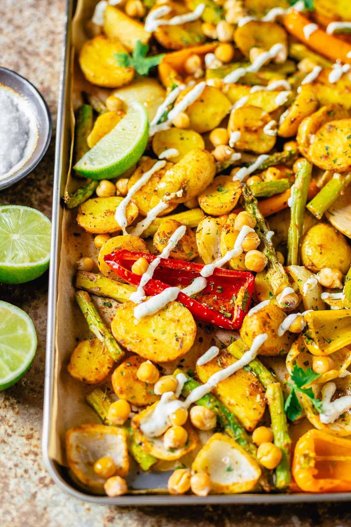 baked vegetables in a sheet pan drizzled with vegan white dressing