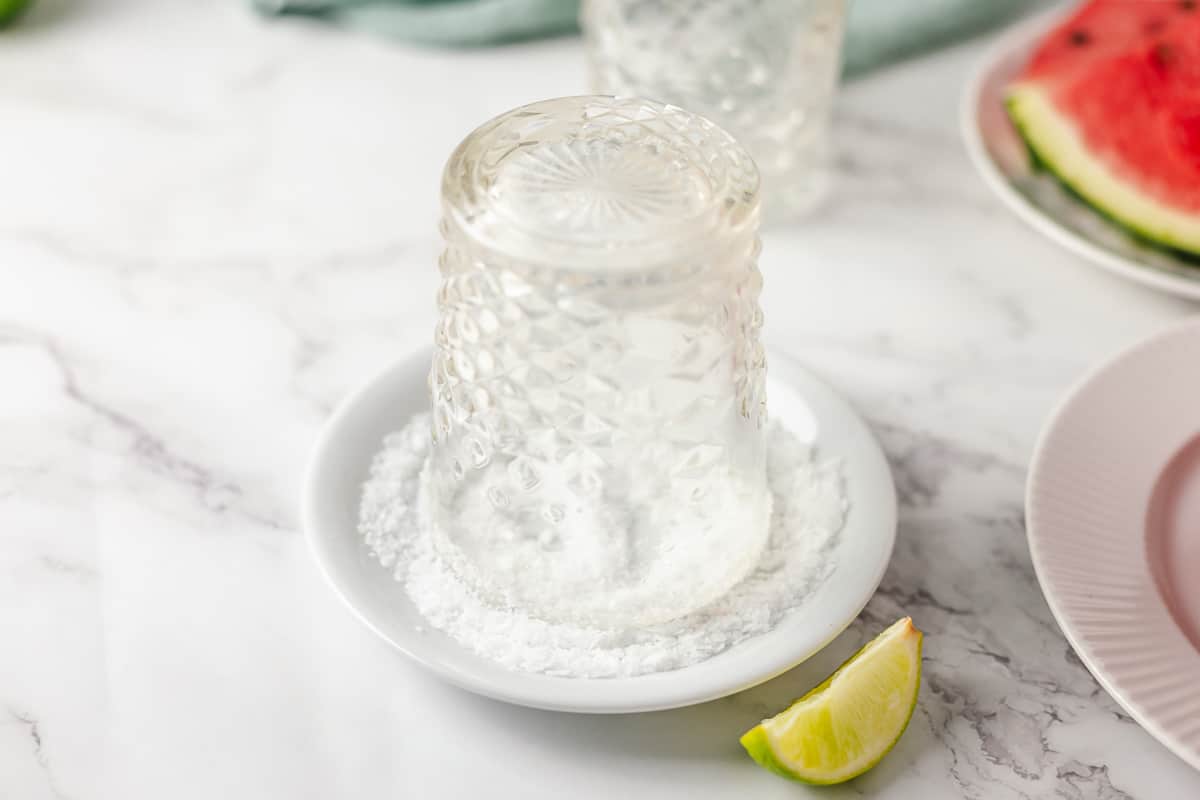 Prepare the whiskey glass by dipping the top of it in crushed sea salt flakes